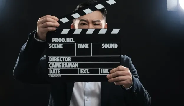 A person holds a film clapperboard in front of their face, preparing to start a scene on a dark background.
